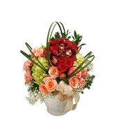 Arrangement of cymbidium orchids, peach roses, red roses, baby's breath and more in a white basket